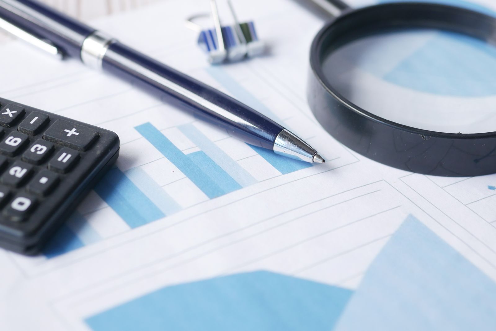 Een rekenmachine, een pen en een vergrootglas op financiële documenten, symbool voor het natrekken van een bedrag